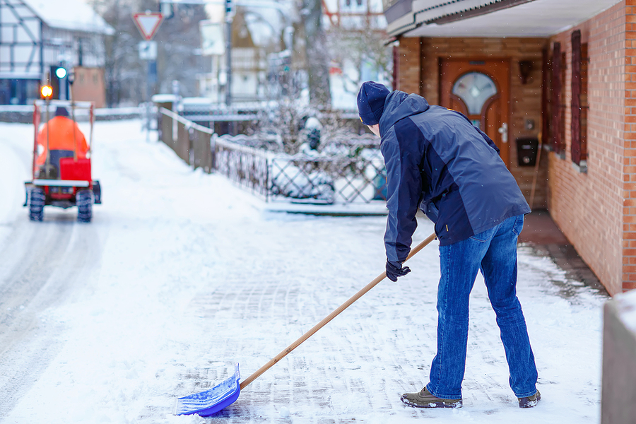 Man with snow shovel cleans sidewalks in winter during snowfall. Winter time in Europe. Young man in warm winter clothes. Snow and weather chaos in Germany. Snowstorm and heavy snowing. Schneechaos